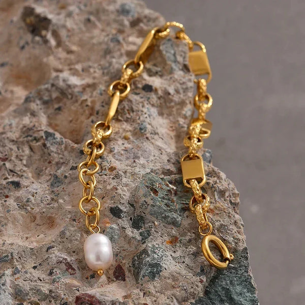 Gold chain earring with a pearl on a textured stone surface