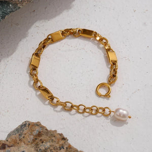 Gold chain bracelet with a pearl on a textured surface