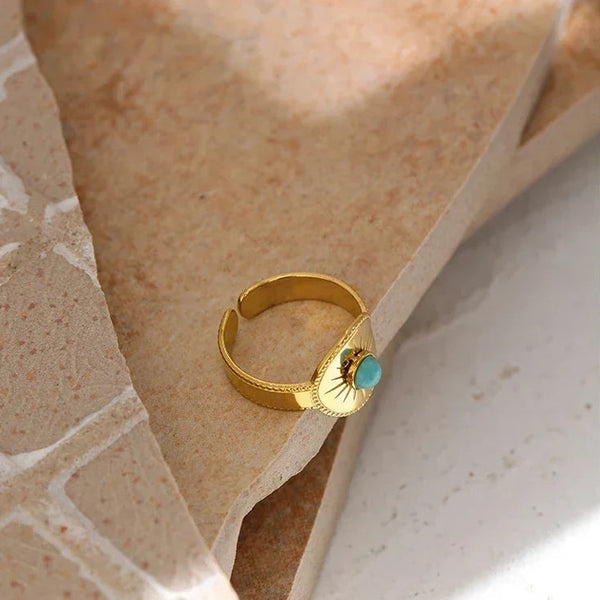Gold-plated adjustable ring with turquoise gemstone on textured stone background