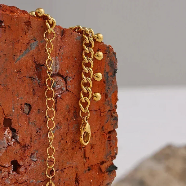 Gold chain necklace on a textured orange surface with 'DESIGN DETAILS' text.