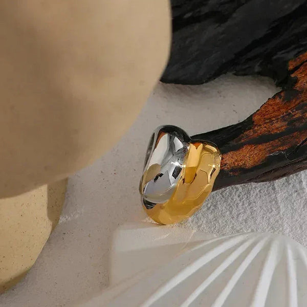 Chunky two-tone gold and silver ring on textured white surface with organic elements