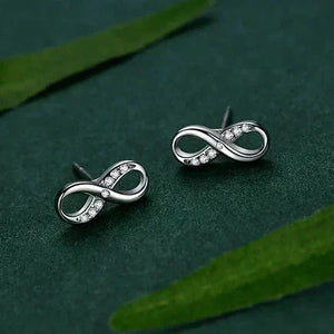 Silver infinity symbol earrings on a green leafy background