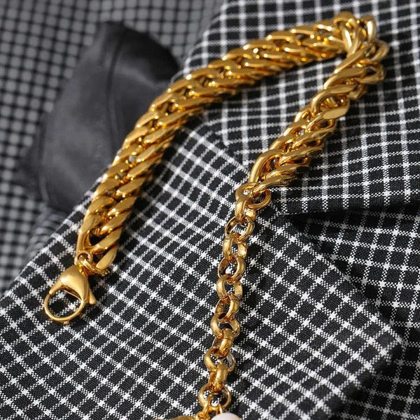 Gold chain bracelet with a shell and pearl charm on a checkered fabric background