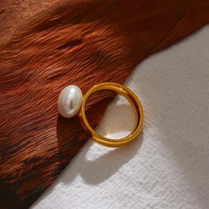 18K gold-plated ring with a white pearl accent on wood and fabric background