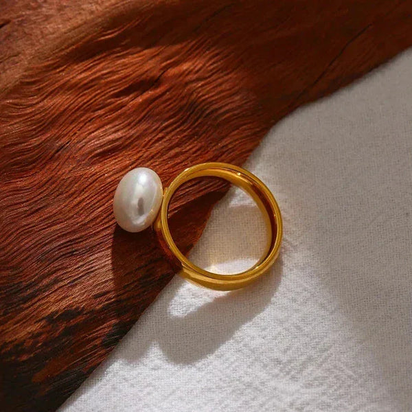 18K gold-plated ring with a white pearl accent on wood and fabric background