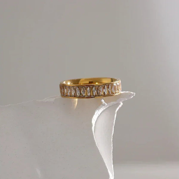 18K gold-plated ring with baguette-cut clear stones on a white textured surface