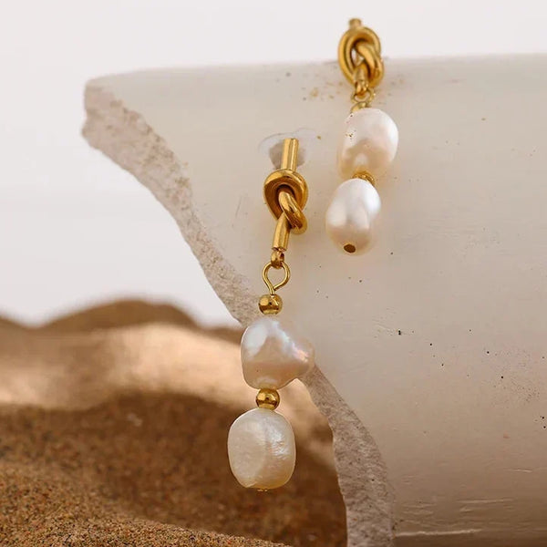 Pearl and gold earrings on a shell with sand and water background