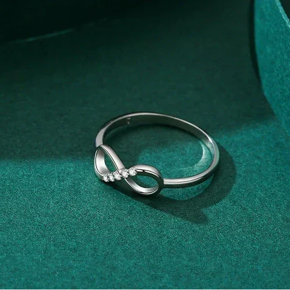 Silver infinity ring on a teal surface with 'Real Shotshow' text above.