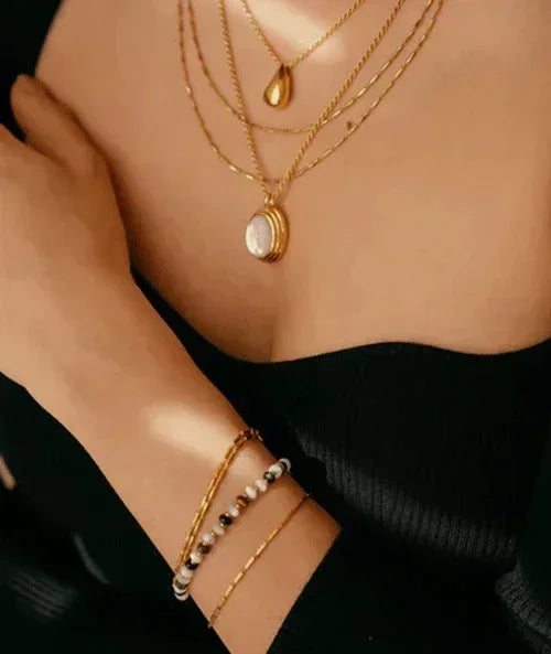 Close-up of a person wearing multiple gold necklaces and bracelets on a dark background