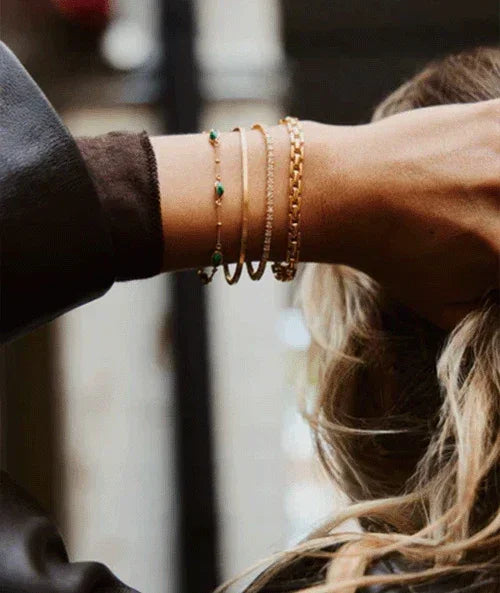 Layered gold chain bracelets on a wrist, showcasing the stylish connections of TM & Co. Jewels' collection.
