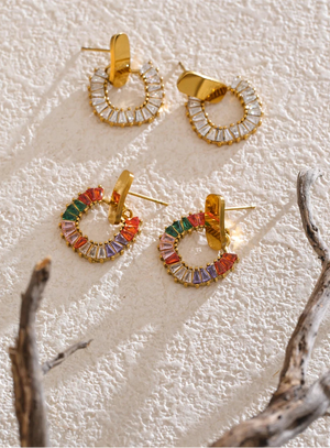 Gold hoop earrings with colorful stones on a textured white surface.
