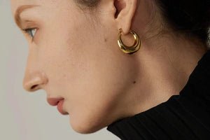 Close-up of a person wearing a gold hoop earring against a neutral background