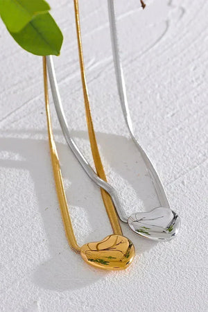 Gold and silver necklaces on a textured white surface with a green leaf.