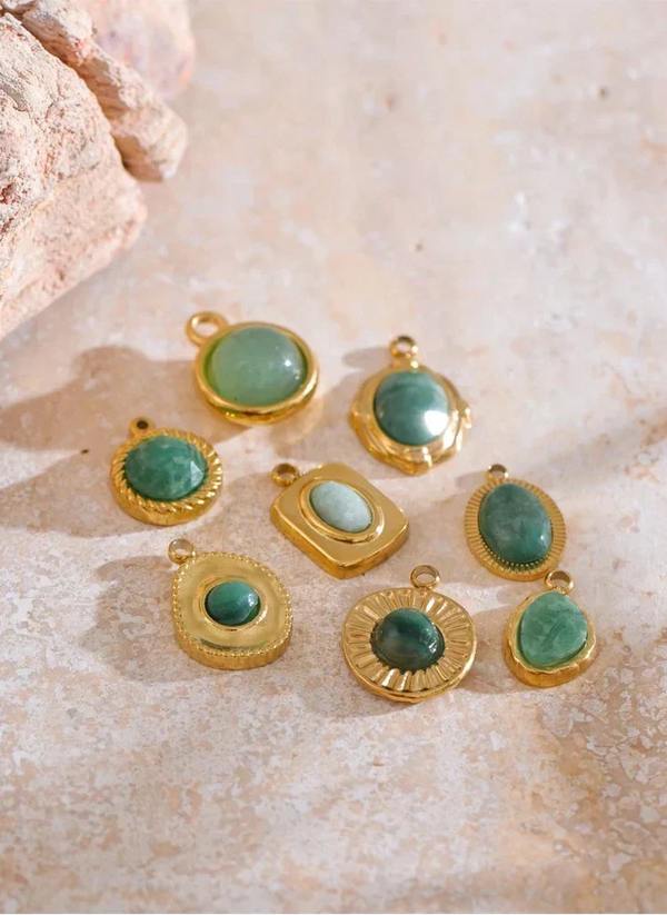 Gold-framed green gemstone pendants on a textured beige surface