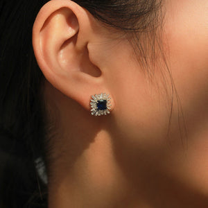 Close-up of an ear wearing a diamond earring with a blue gemstone.