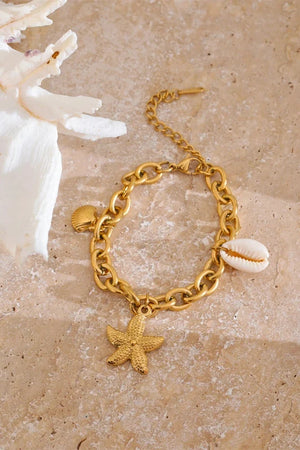 Gold bracelet with starfish and shell charms on a beige surface