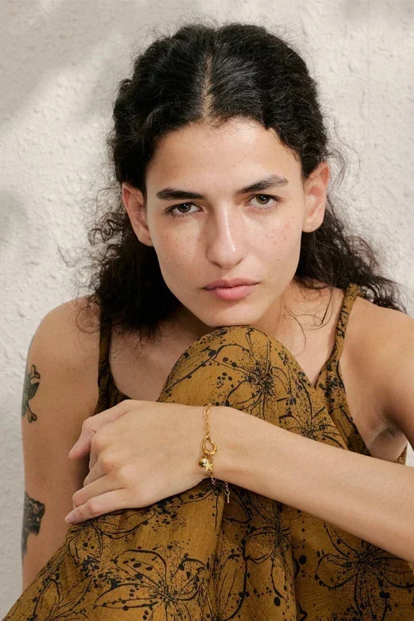 Woman wearing a mustard yellow sleeveless top with black floral patterns against a neutral background