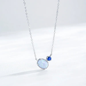 A silver chain necklace featuring a large, teardrop-shaped white opal pendant and a smaller round blue gemstone, displayed on a clean white background.