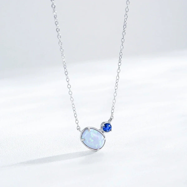 A silver chain necklace featuring a large, teardrop-shaped white opal pendant and a smaller round blue gemstone, displayed on a clean white background.