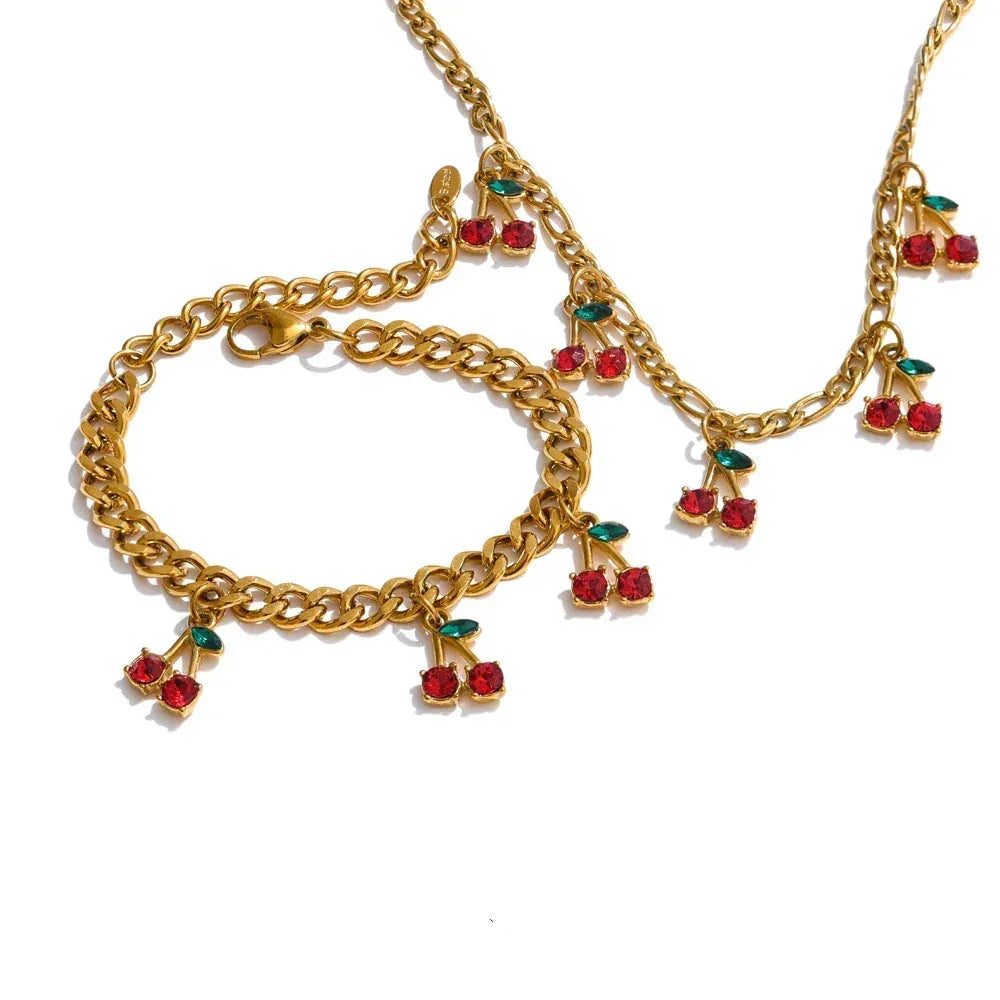 Gold chain bracelet with red and green gemstone charms on a white background.
