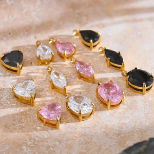 Gold-framed gemstone pendants on a textured beige surface