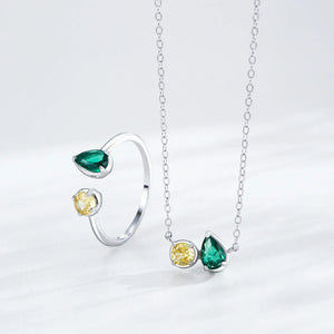 Silver ring and necklace set with green and yellow gemstones on a light gray background