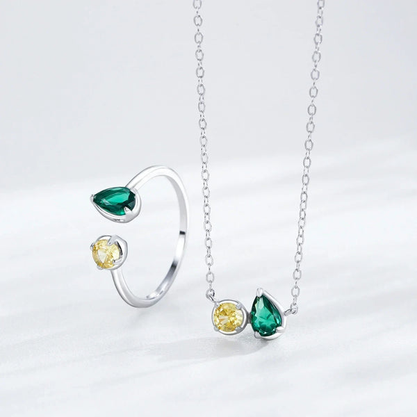 Silver ring and necklace set with green and yellow gemstones on a light gray background