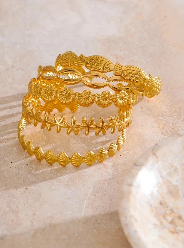Set of gold rings with intricate designs on a beige shell background