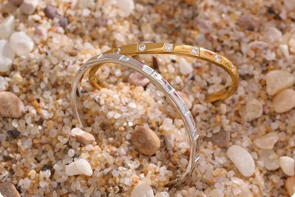 Gold and silver bangle bracelets with cubic zirconia stones on beige fabric