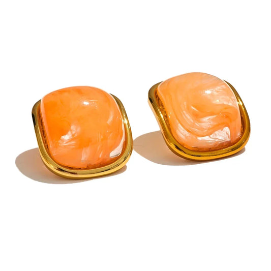 Pair of orange earrings with gold frames on a white background