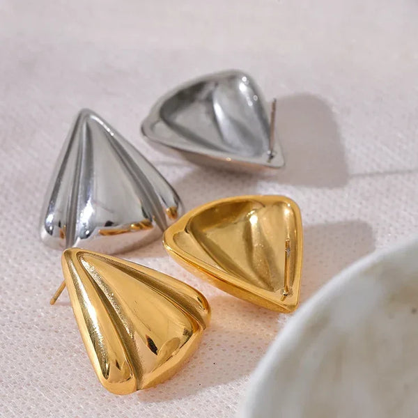 Gold and silver cone-shaped earrings on a light pink surface.