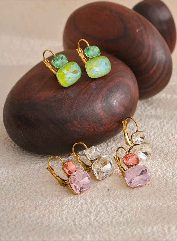 Pair of earrings with colorful gemstones on wooden and stone background