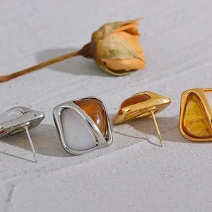 Four earrings in different colors on a textured surface with a dried flower.