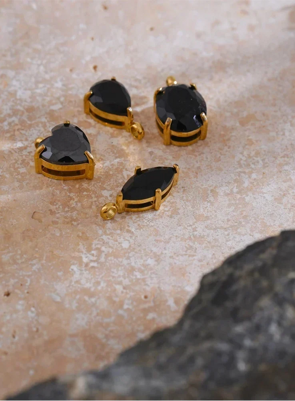Four black teardrop-shaped gemstones with gold prongs on a beige stone surface.