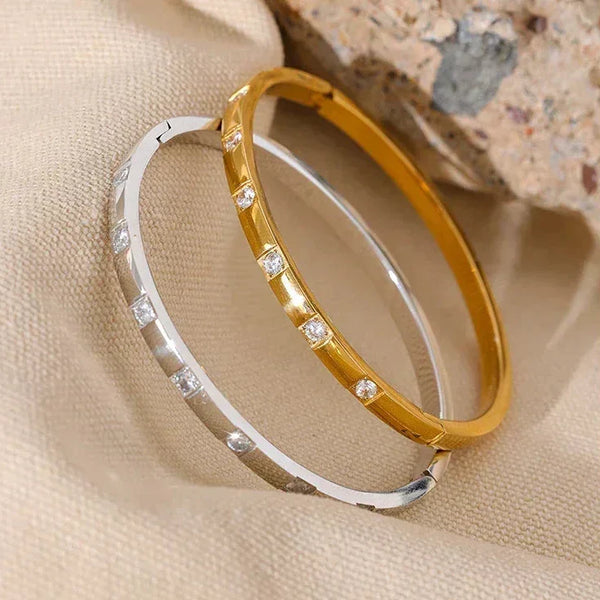 Gold and silver bangle bracelets with cubic zirconia stones on beige fabric