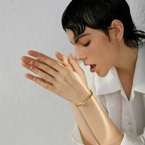 Woman in white shirt wearing gold-plated bangle bracelet, minimal and elegant style.