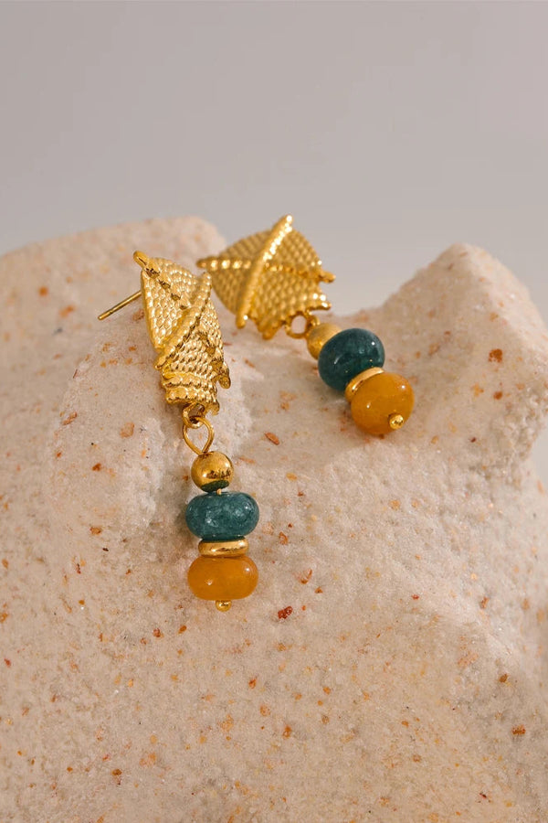 Gold earrings with green and yellow beads on a textured beige surface