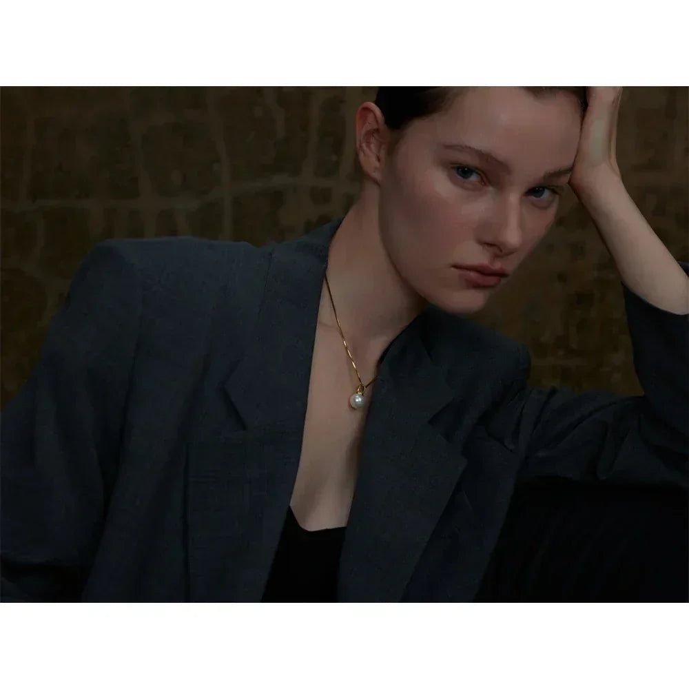 Woman wearing a dark blazer with a pearl necklace against a blurred background