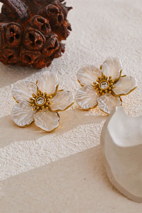 Floral earrings with gold centers on a textured surface with a vase and decorative object.