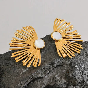 Gold earrings with a central pearl on a gray stone surface, branded as Vogue.