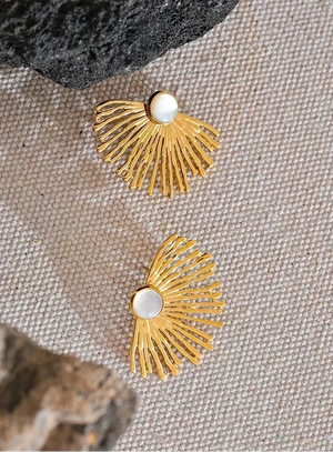 Gold earrings with a central pearl on a textured fabric background