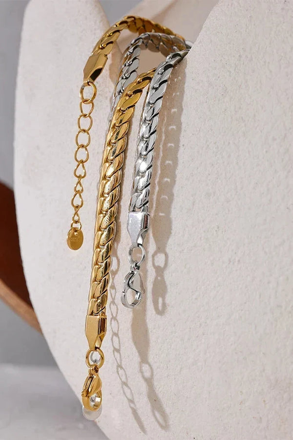 Three gold and silver chain bracelets on a white surface.
