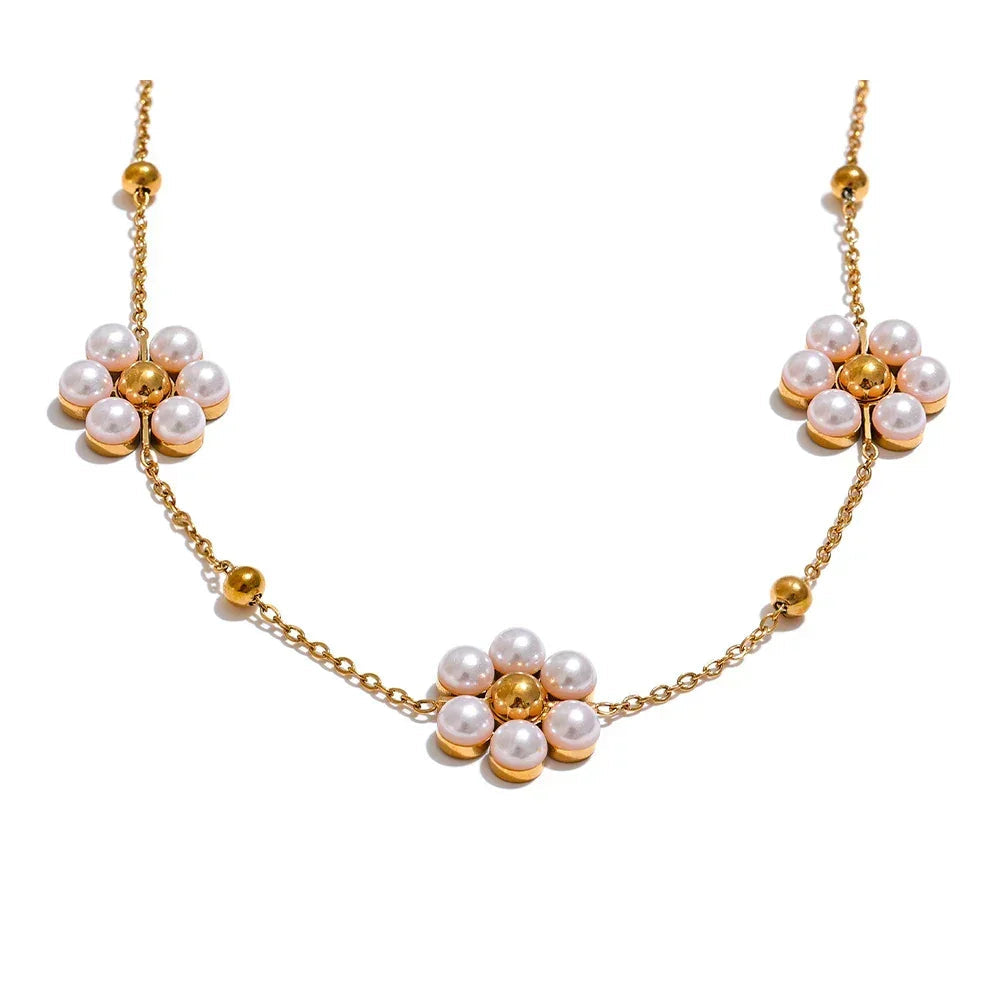 Gold necklace with floral designs and pearls on a white background.