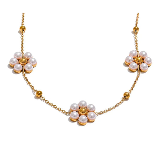 Gold necklace with floral designs and pearls on a white background.