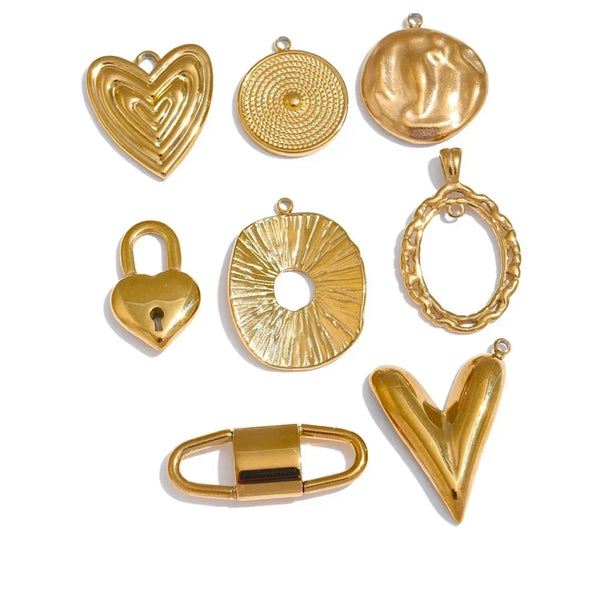 A set of nine gold-toned metal jewelry charms and pendants arranged on a plain white background, including multiple heart, oval, circular, and padlock-shaped designs.