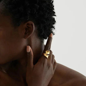 Woman wearing a bold 18K gold-plated statement ring on her finger, minimal background