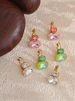 Set of colorful gemstone earrings on a textured surface with a wooden object.