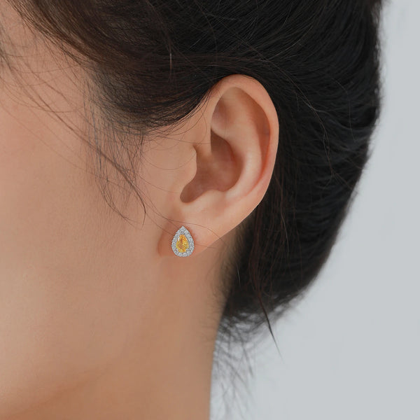Close-up of an ear wearing a silver earring with a yellow gemstone on a blurred background