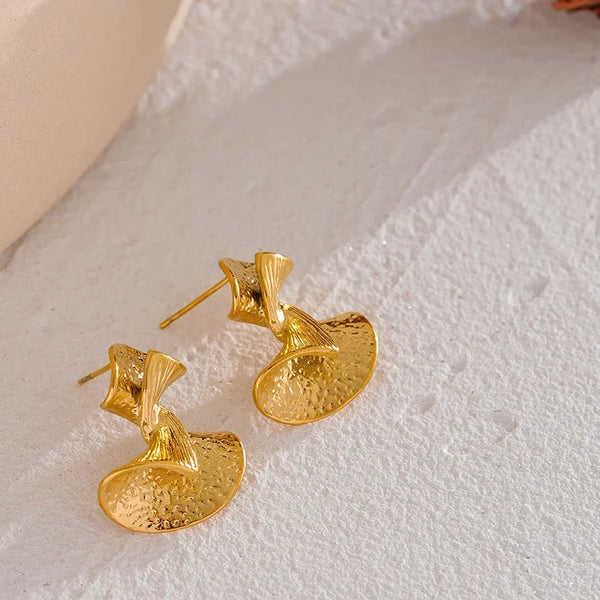 Gold earrings on a textured white surface with 'Vogue' branding.