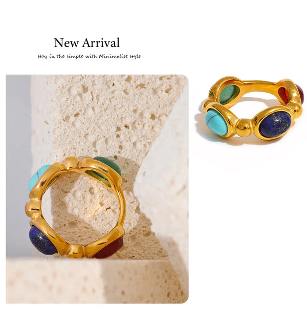 Gold-plated ring with red, green, and blue gemstones on textured stone background